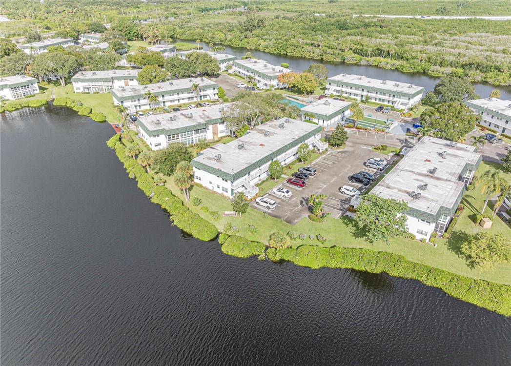 Waterfront complex featuring manicured grounds, paved surface parking, and mature trees