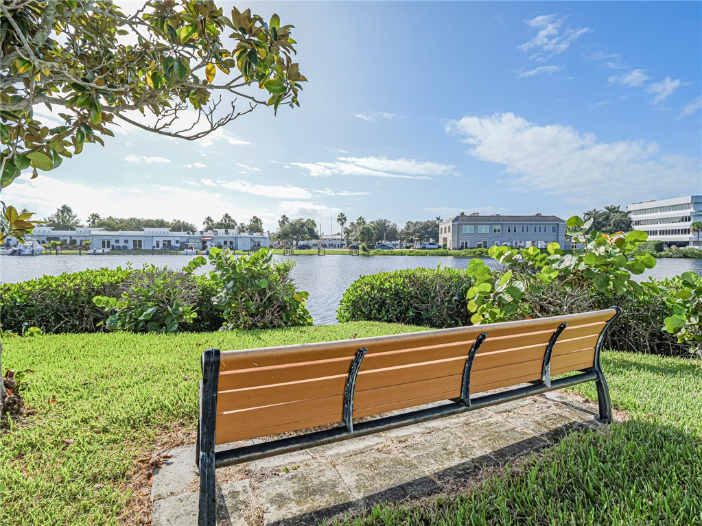 Waterfront property grounds featuring a concrete paver pad, manicured lawn, established shrubs, and mature tree canopy