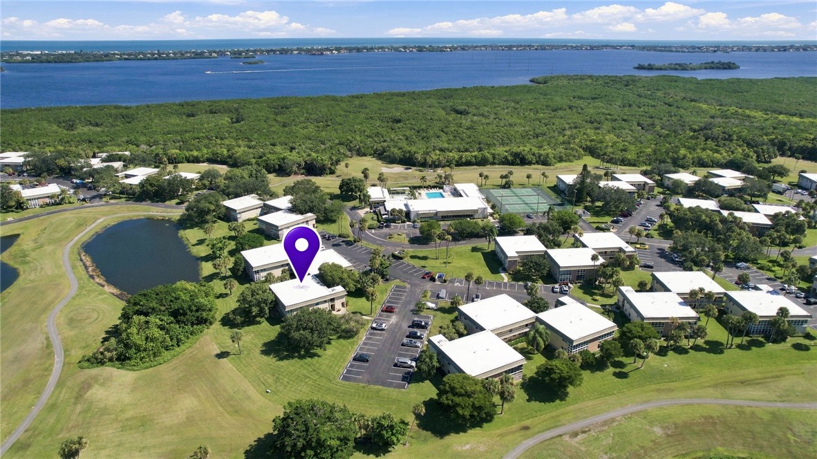 Aerial perspective of a multi-unit complex featuring an outdoor swimming pool, tennis court, communal parking areas, and mature landscaping
