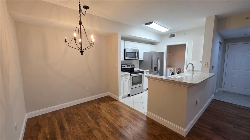 Kitchen featuring white cabinetry, stone-finish countertops, stainless steel appliances, and wood-finish flooring, complemented by an ornate metal chandelier