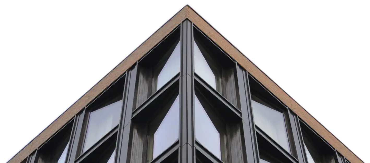 Close-up of the sharp corner of a modern building featuring large reflective glass windows framed by dark metal and topped with a light brown brick edge.