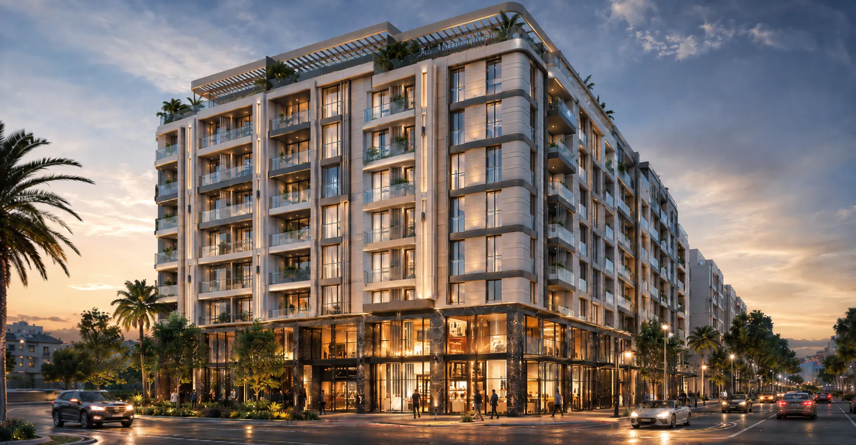 Modern multi-story residential building with balconies and glass storefronts on the ground floor, illuminated at dusk with palm trees and cars on the street.