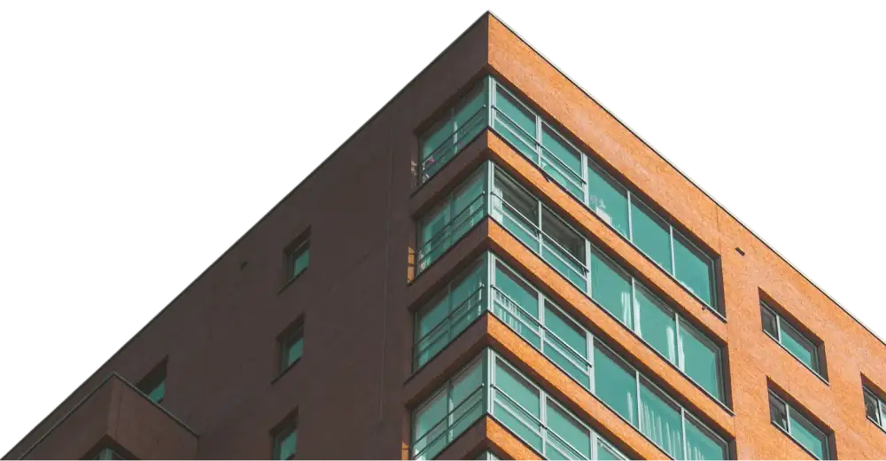 Orange brick building corner with several rows of large reflective glass windows and metal railings, against a black background.