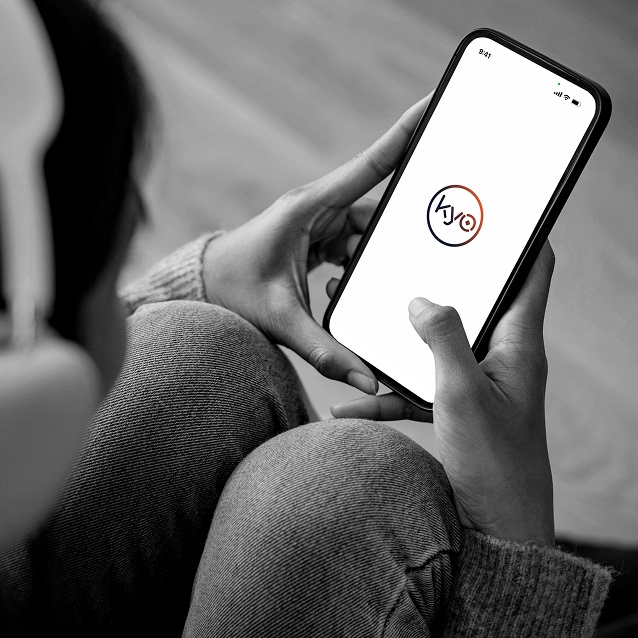 Person holding a smartphone displaying the project’s circular logo on a white screen, shown in a black-and-white lifestyle mockup.