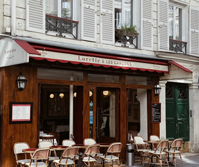 Charming Parisian café storefront with red awnings, wooden doors, and outdoor bistro seating along the sidewalk.