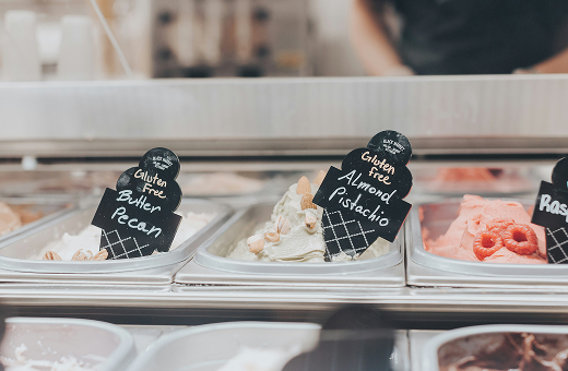 Gelato display case featuring assorted flavors, including butter pecan, almond pistachio, and strawberry, labeled with handwritten flavor signs.