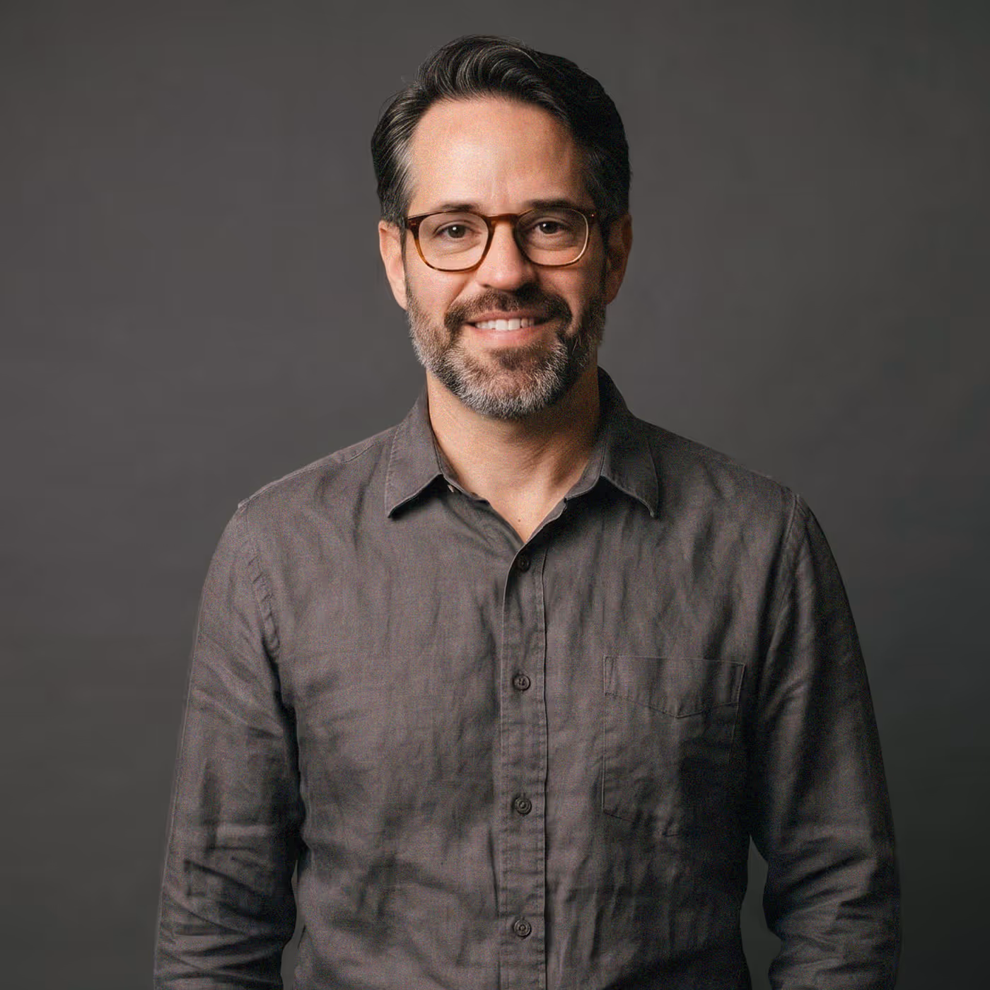 Jesse Douma, founder of Guidepost Digital, smiling in glasses and a charcoal linen shirt against a dark grey studio backdrop.