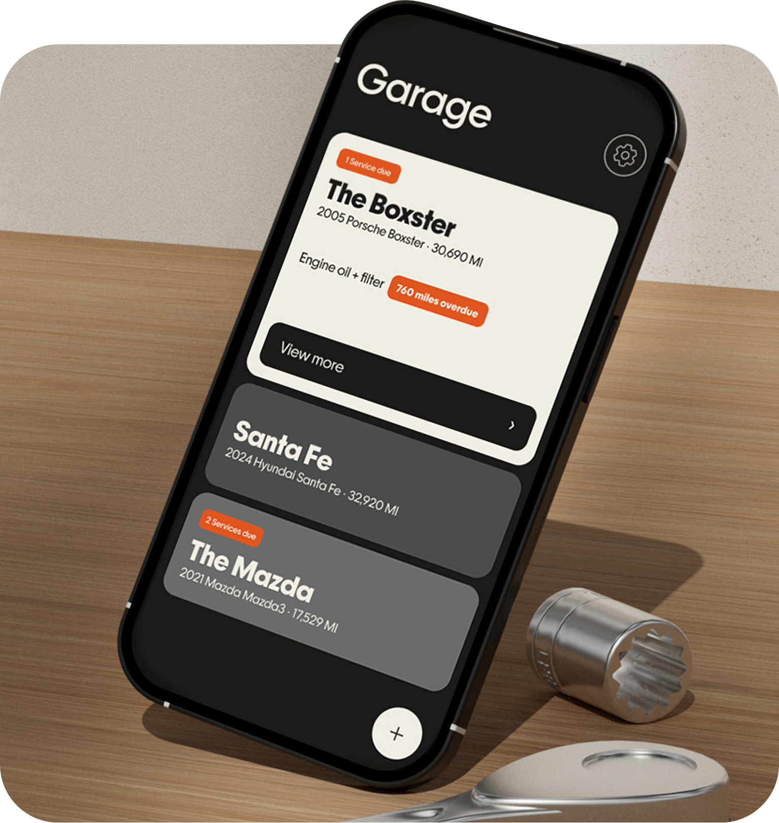 Kept on an iPhone standing on a workbench: the Garage screen with a car selected, engine oil 760 miles overdue flagged in orange