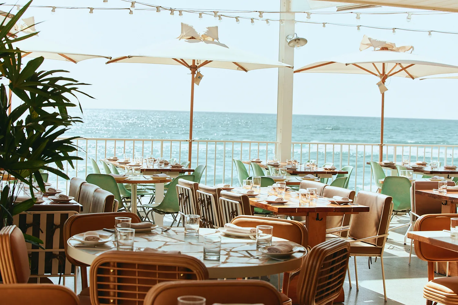 The Tropic terrace with rattan and green chairs under white umbrellas, overlooking the ocean