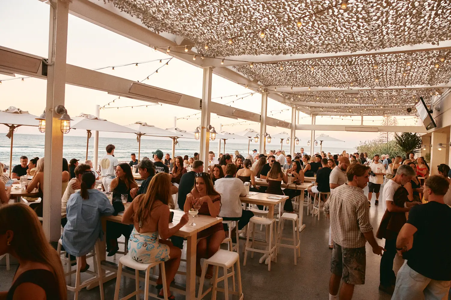 Crowd on the open-air terrace at Burleigh Pavilion at sunset, with the ocean beyond