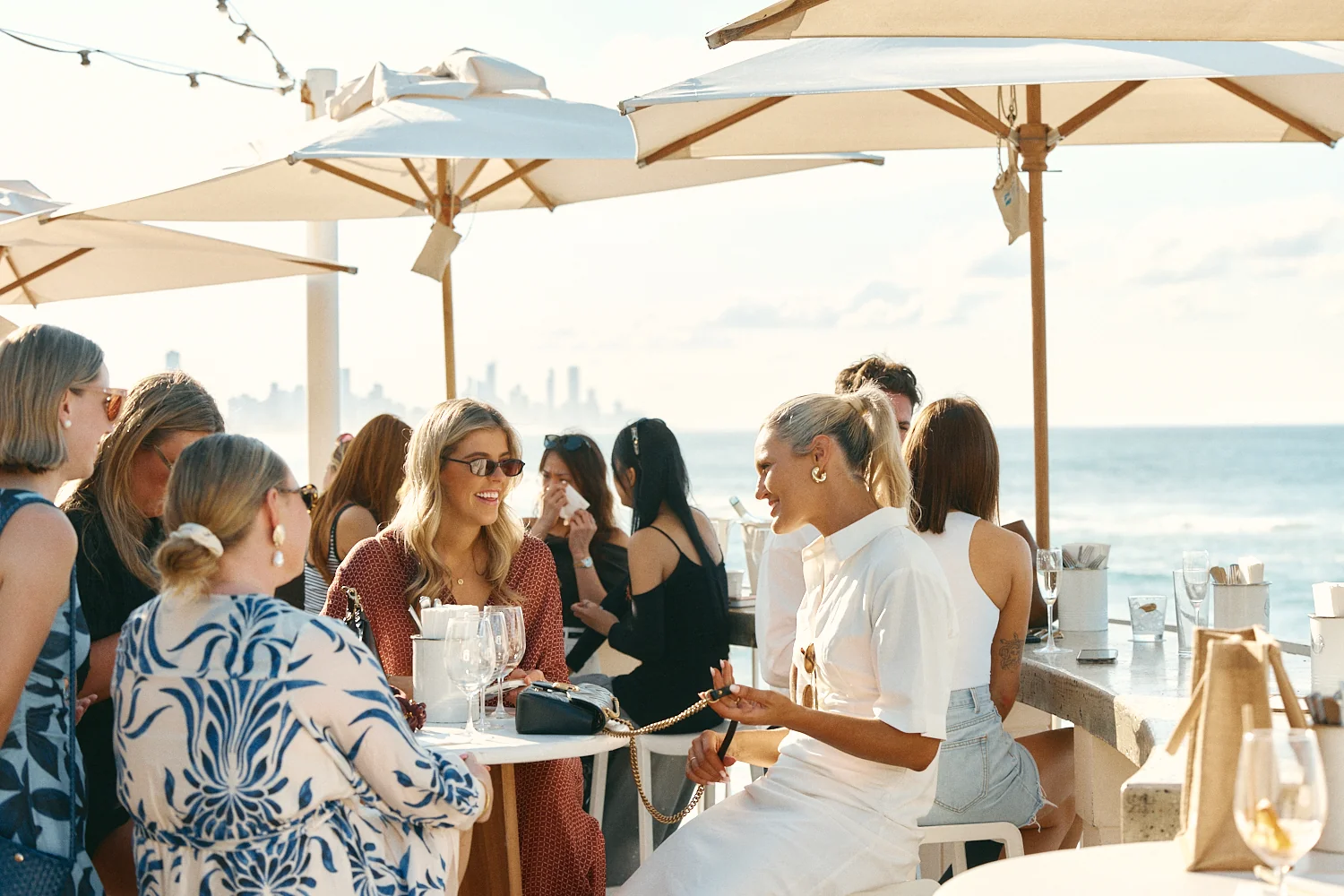 Friends chatting over drinks under umbrellas on the oceanfront terrace