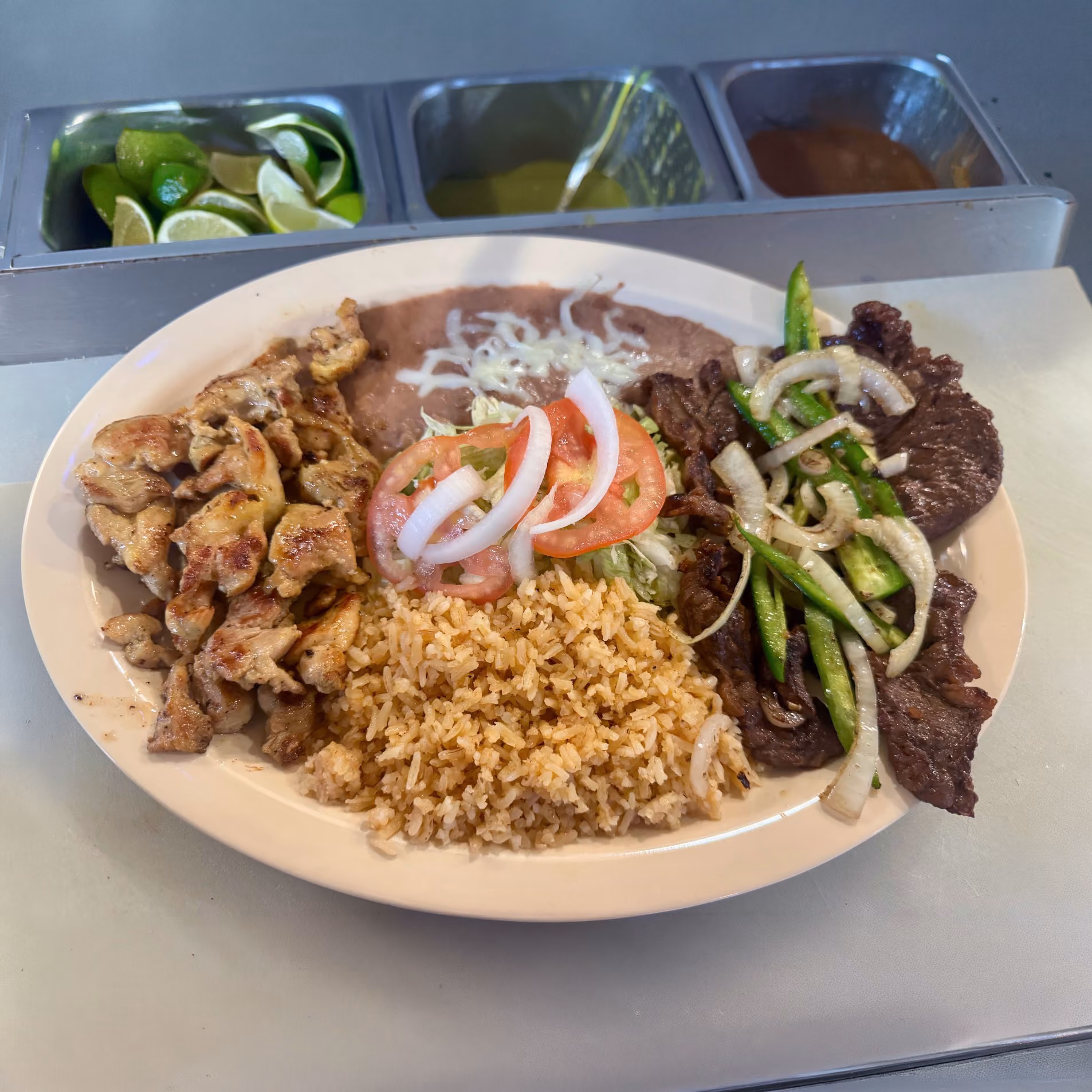 Plate with grilled chicken, grilled steak with onions and green peppers, rice, beans, and salad with tomato and onion.