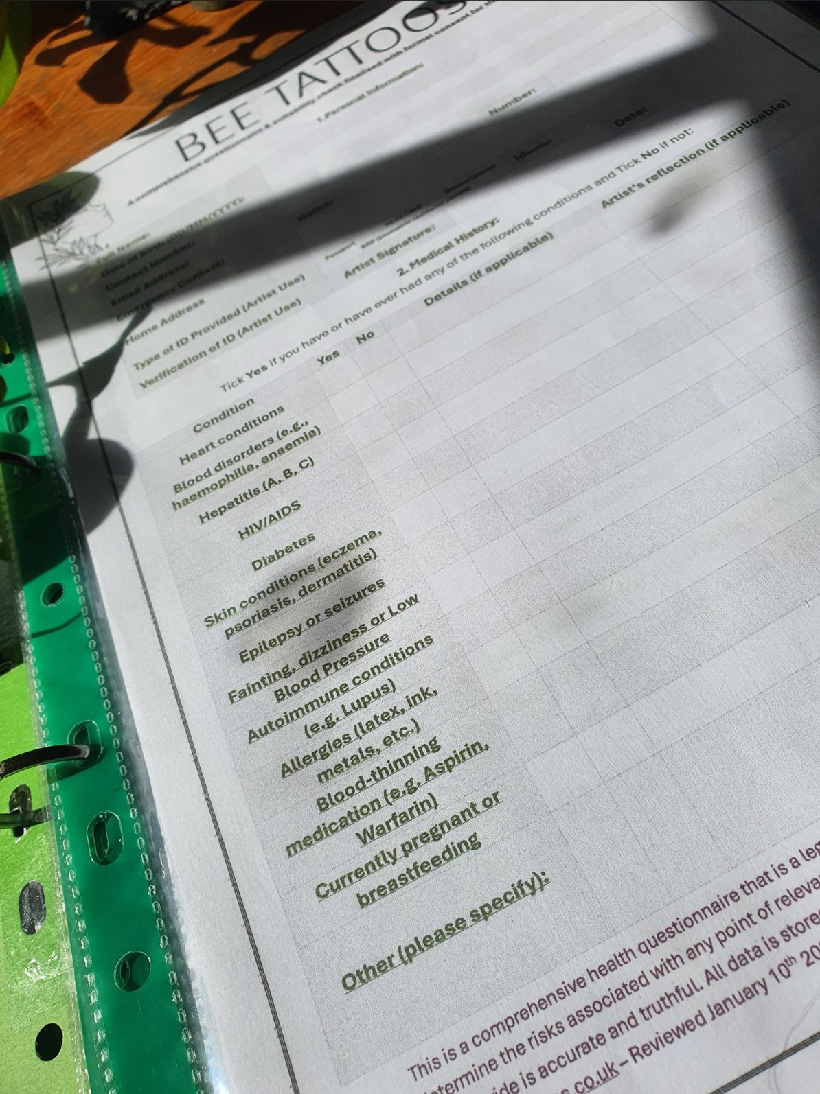 Printed client health questionnaire and consent document for Bee Tattoos listing medical screening conditions and legal declarations in a presentation folder.