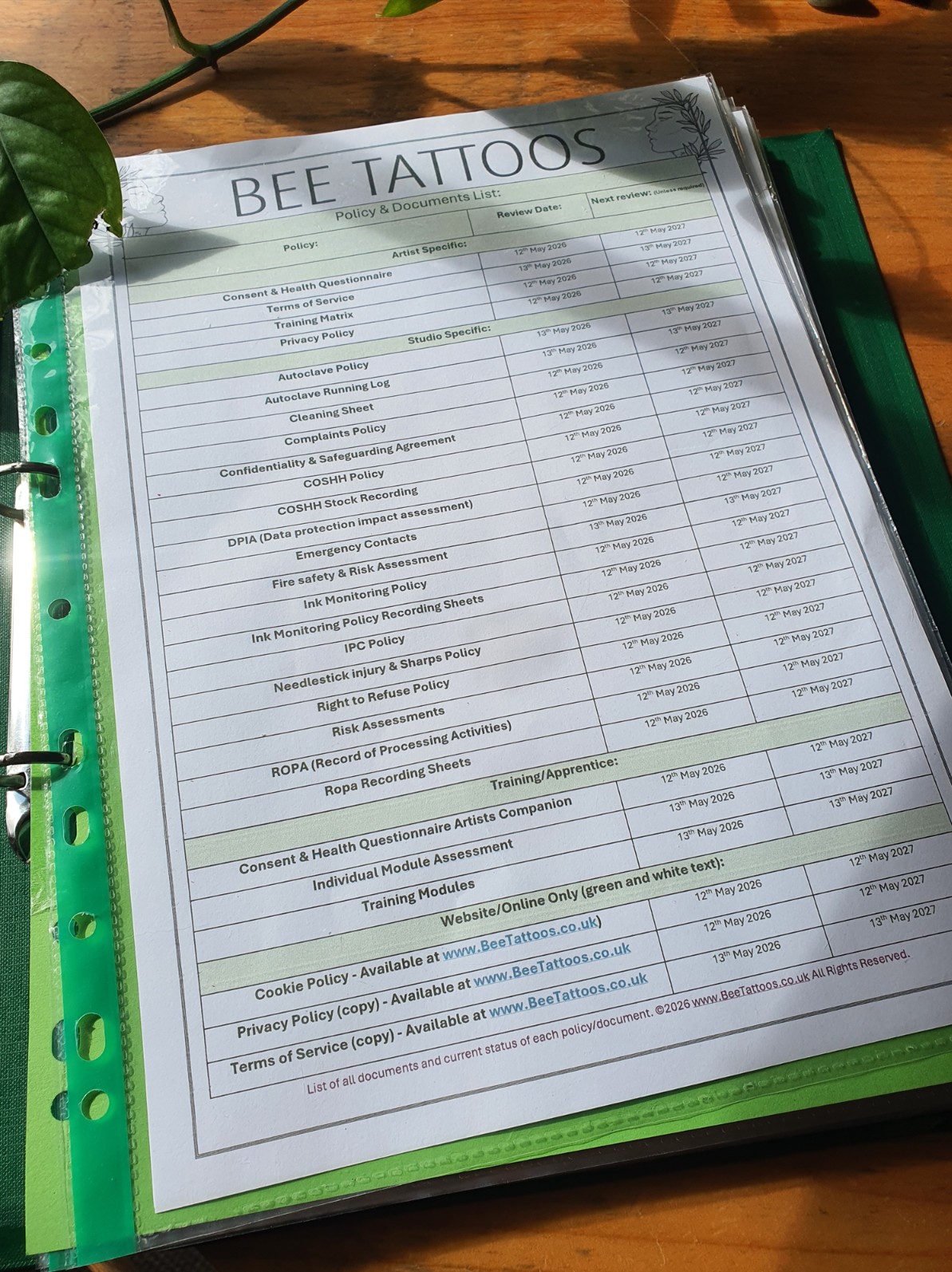 Desk view of the Bee Tattoos compliance manual binder open to the central policy checklist and operational document review matrix.