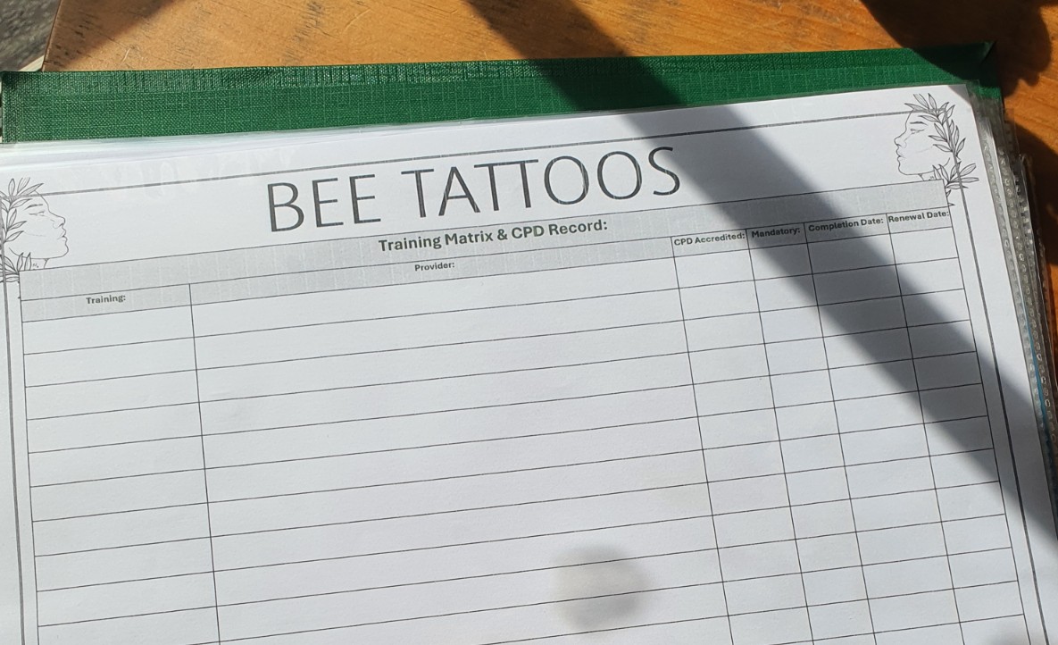 Blank operational training matrix and continuing professional development tracking sheet for Bee Tattoos inside an open green binder.