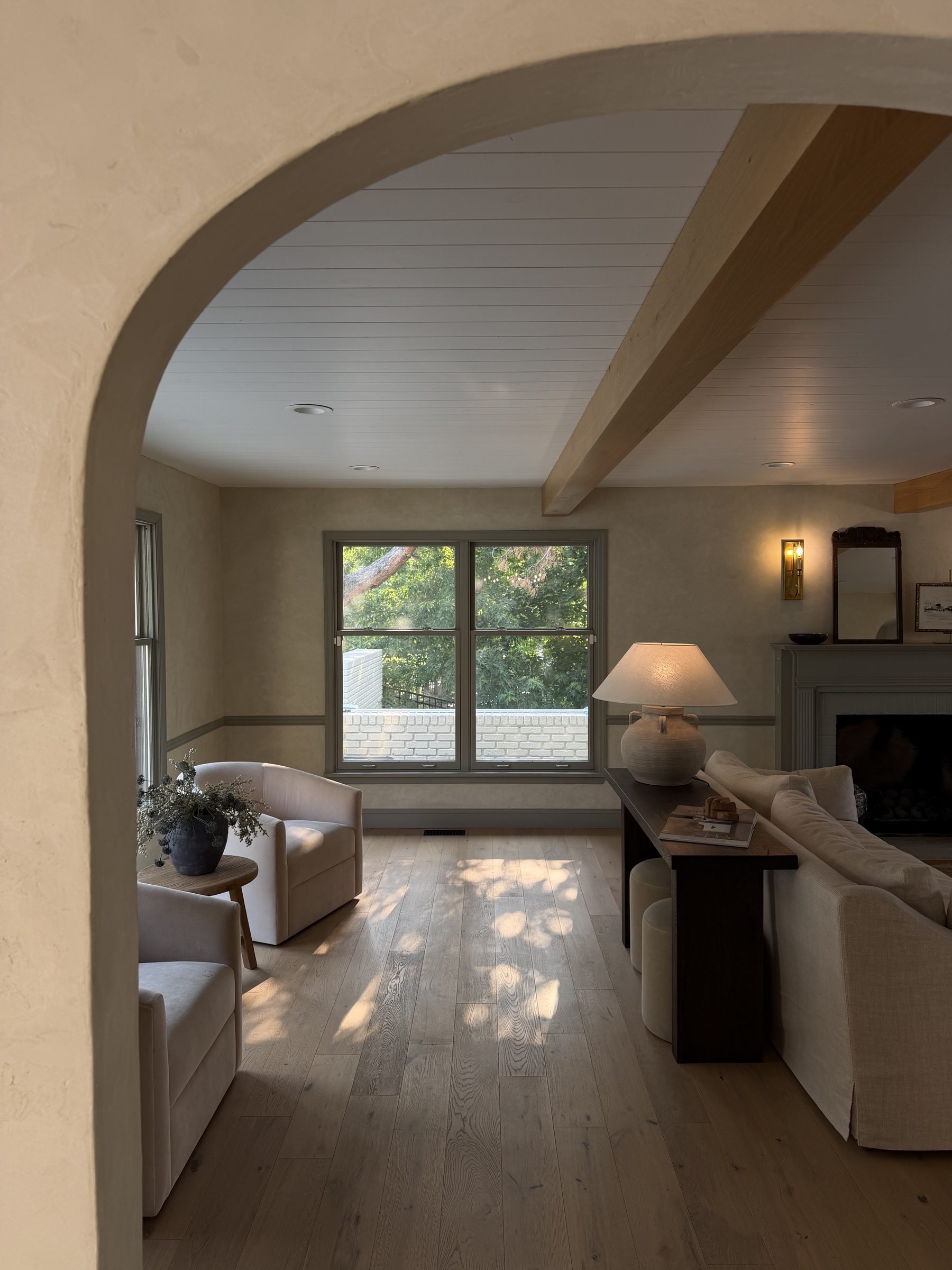 A bare double-hung window with no curtains, framed by a plaster arch, in a neutral living room with white oak floors