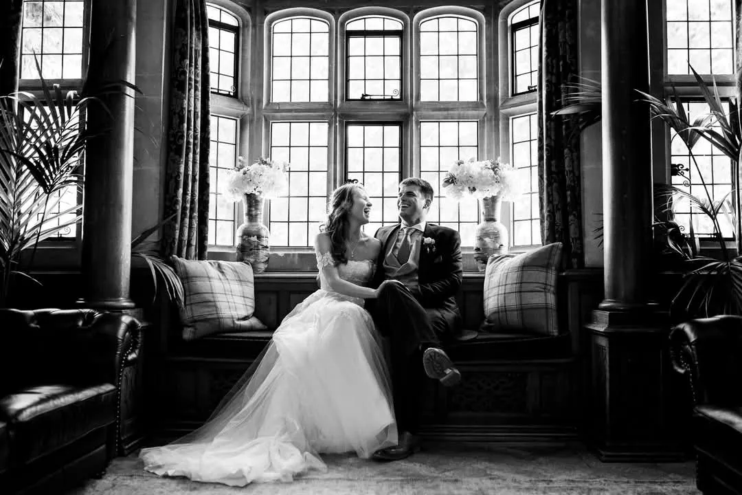 A bride and groom on a window seat in a mullioned bay window at Lanwades Hall