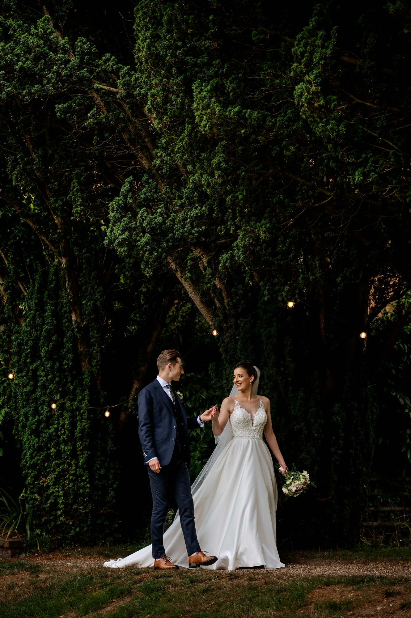 A bride and groom under festoon lights in the garden on a wedding weekend at Lanwades Hall