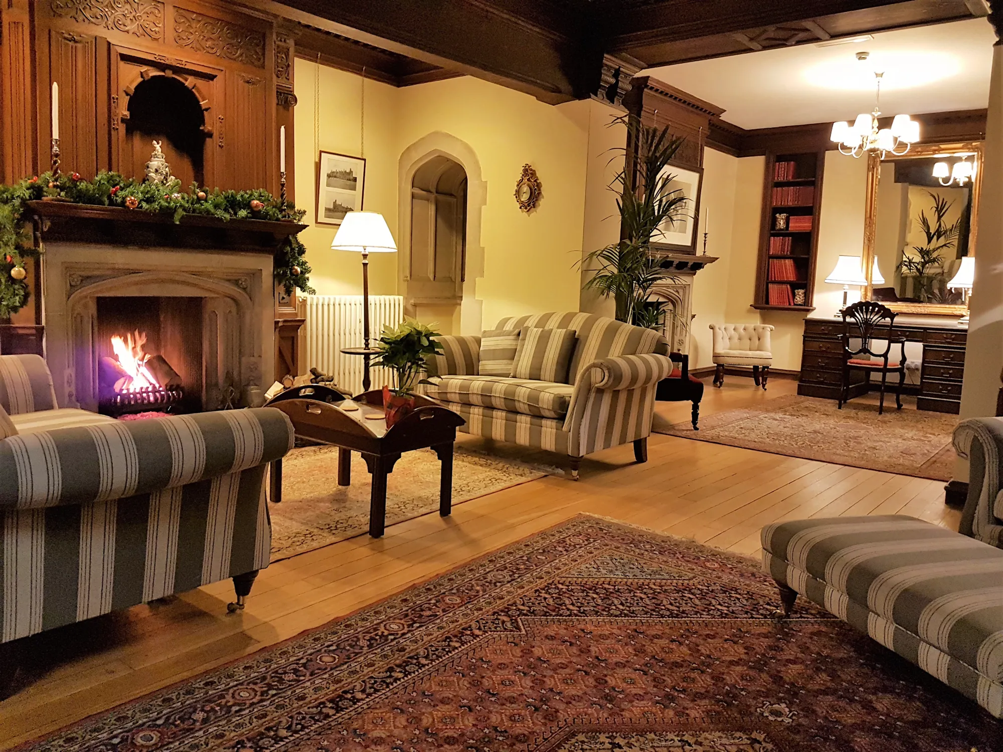 A log fire, garland and striped sofas in a cosy reception room at Lanwades Hall at Christmas