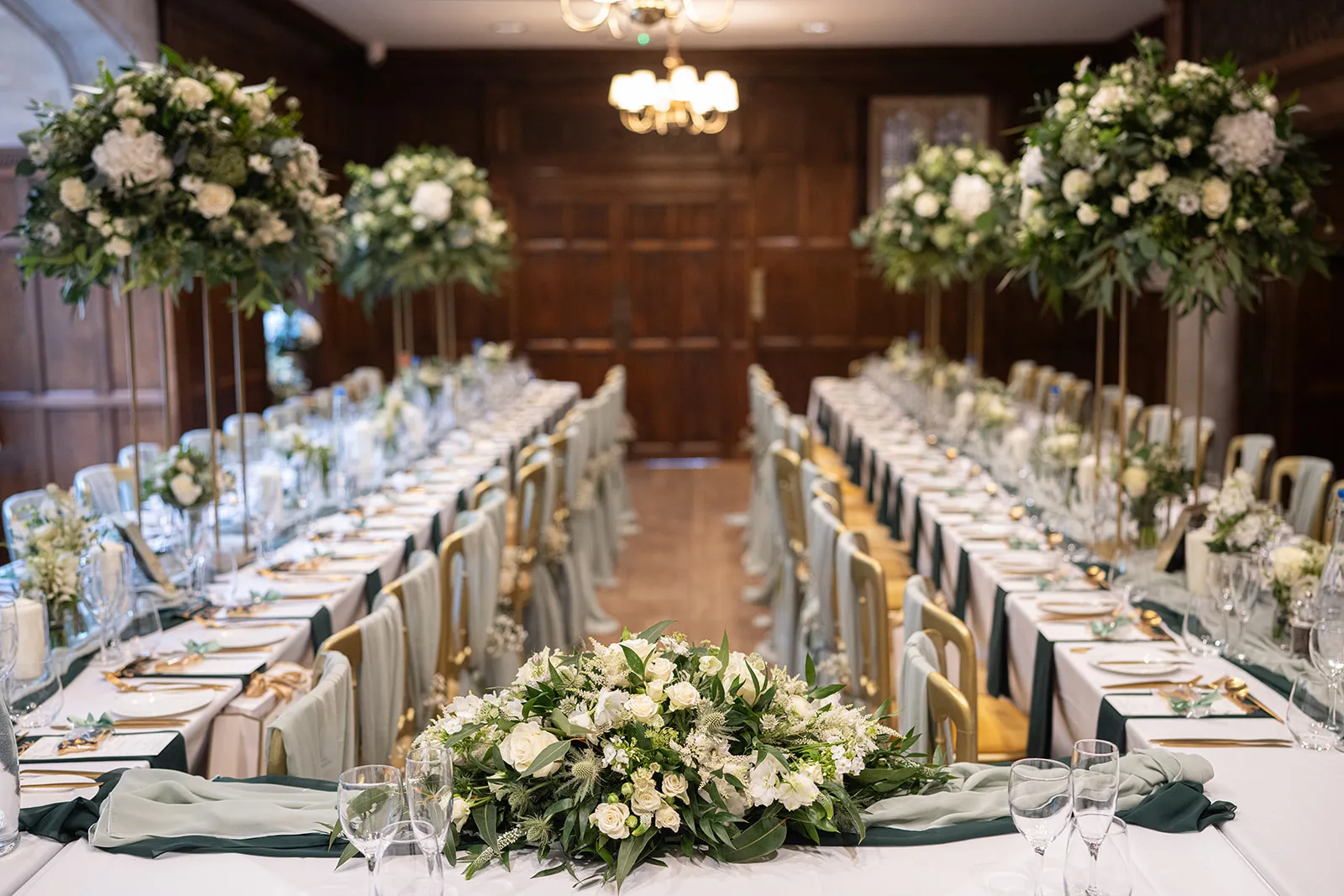 Long tables and tall white flowers set for the wedding breakfast in the Great Hall at Lanwades Hall