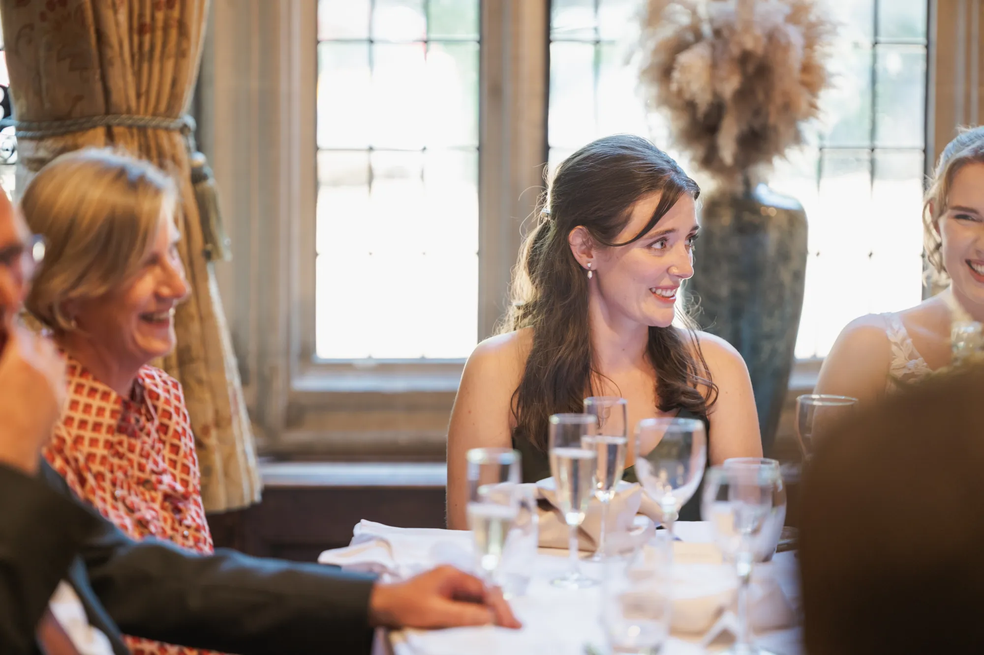 Guests smiling at the wedding breakfast beside tall leaded windows at Lanwades Hall