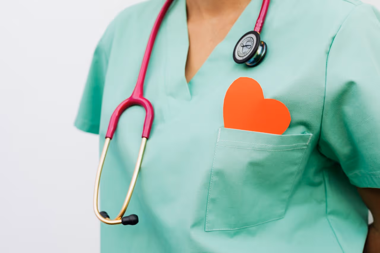 Healthcare professional wearing green scrubs with a red heart shape in the chest pocket and a red stethoscope around their neck.