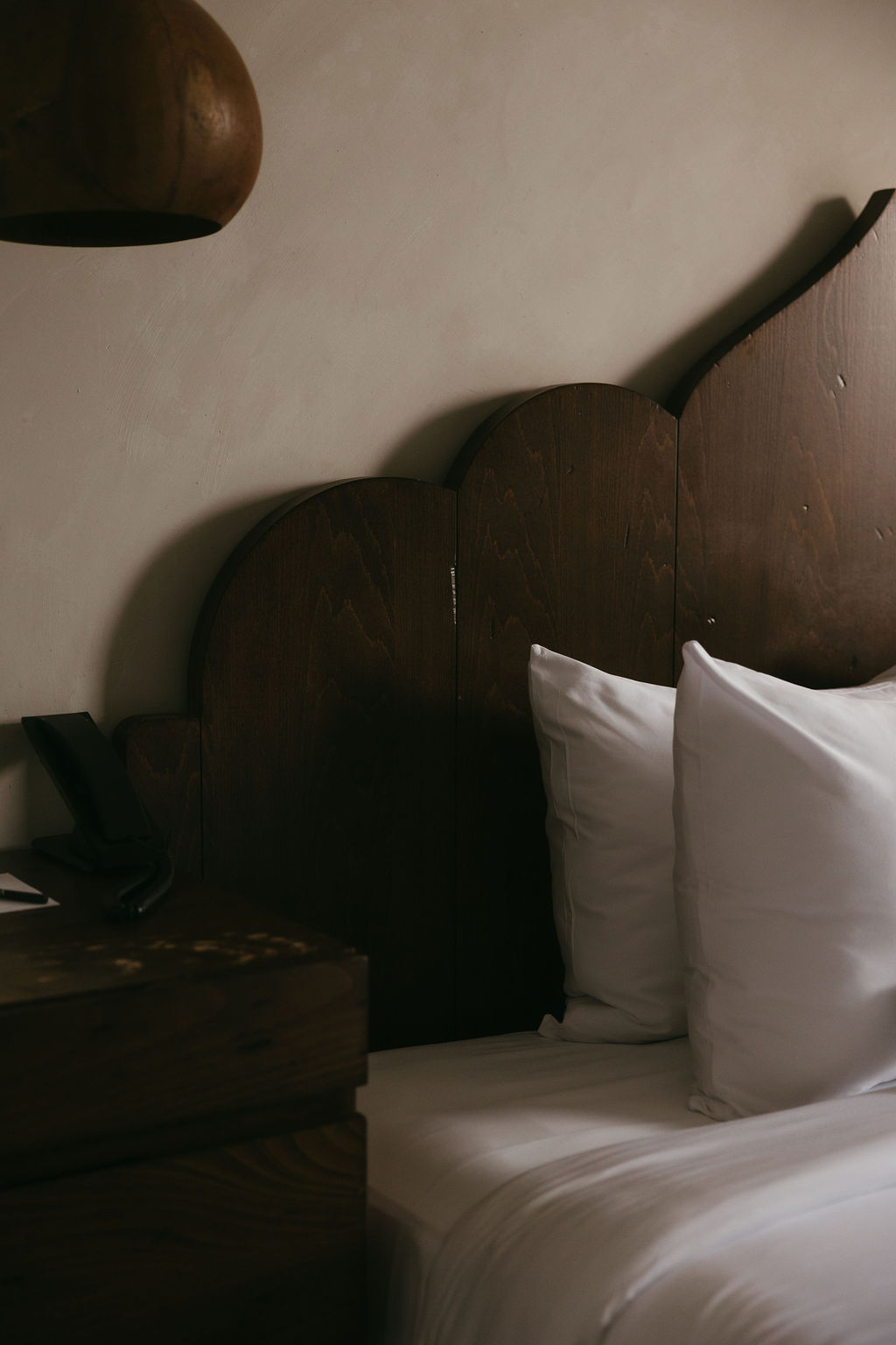 A dark scalloped wood headboard above crisp white pillows