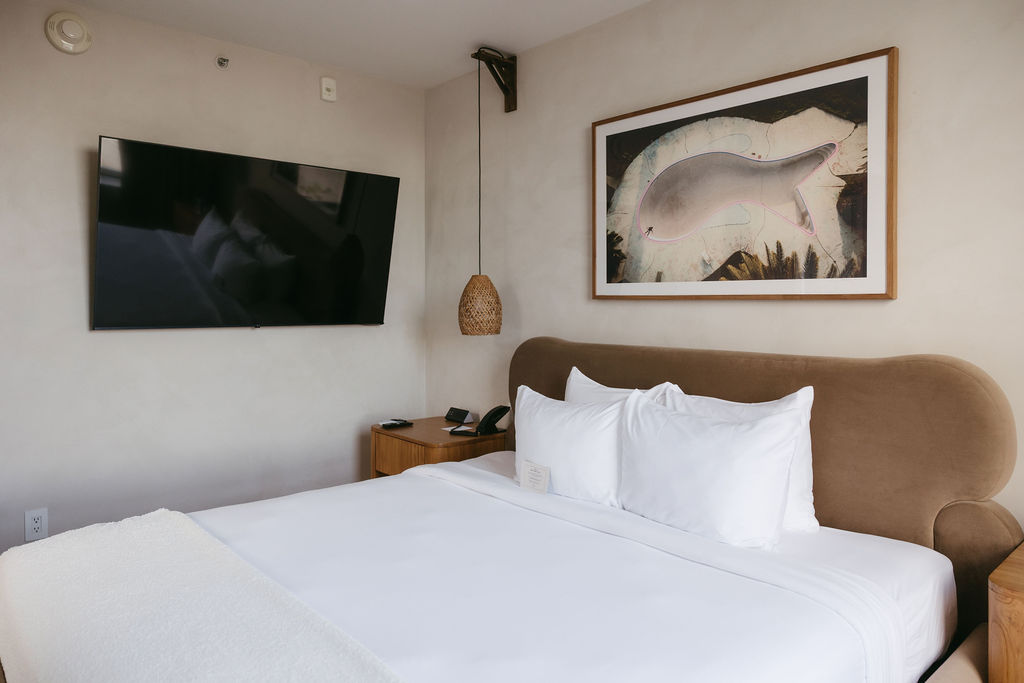 A guest room with a tan velvet headboard, wall-mounted television and framed artwork