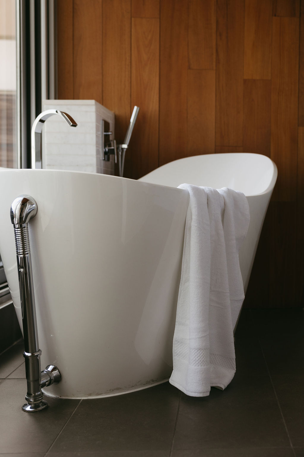 A freestanding tub against walnut panelling, with a towel over the rim