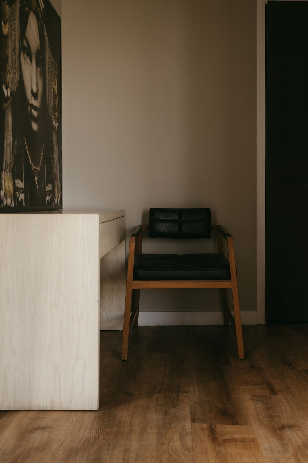 A pale wood desk and black leather chair beside a portrait canvas