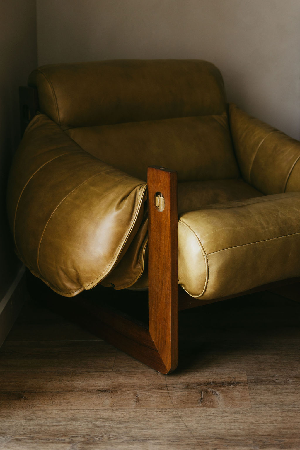 An olive leather lounge chair on a wooden frame