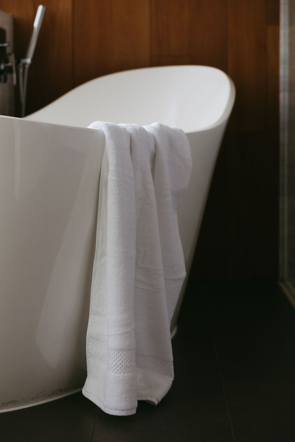 A freestanding soaking tub with a folded white towel, against walnut panelling
