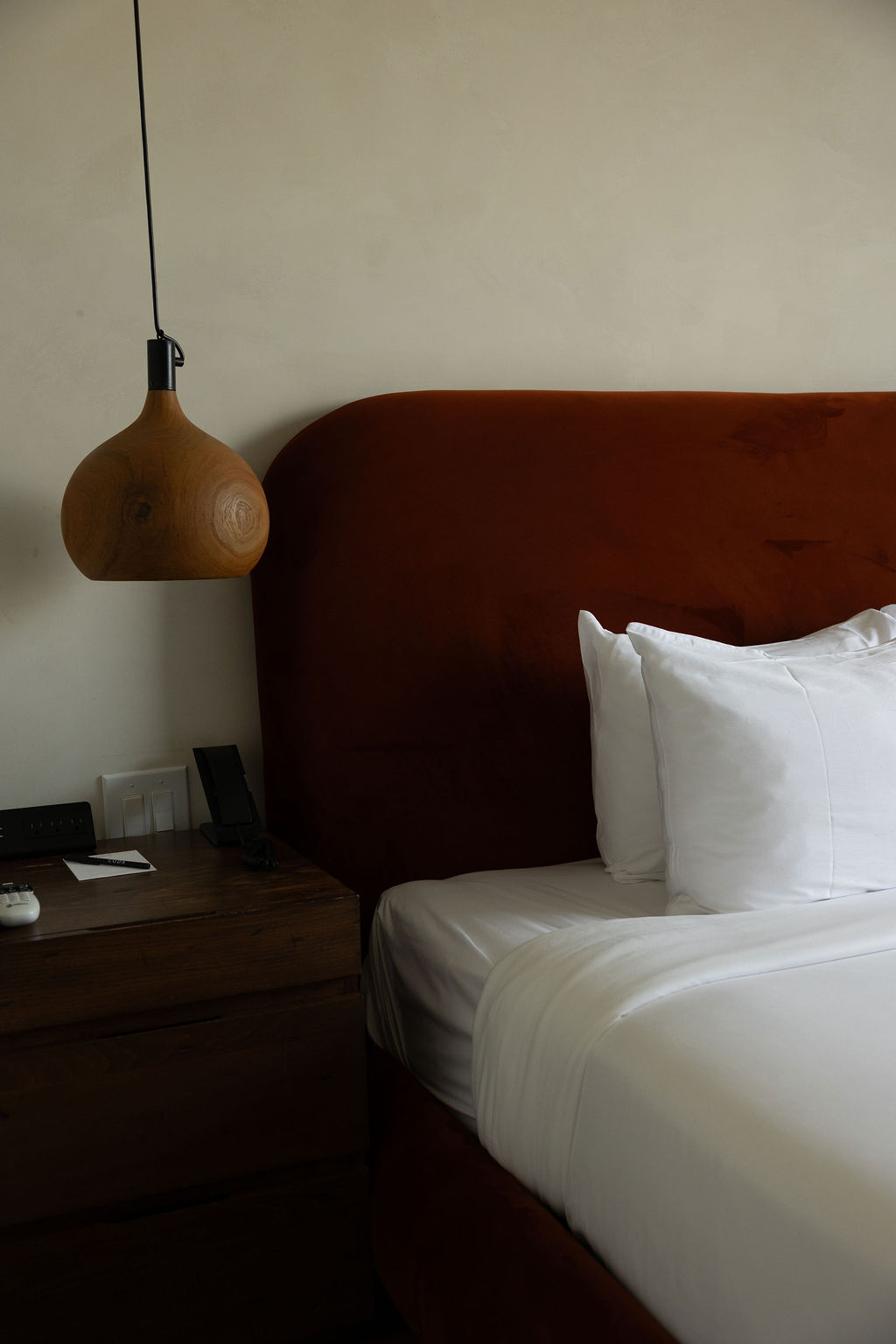 A bed with a rust velvet headboard and a turned-wood pendant light