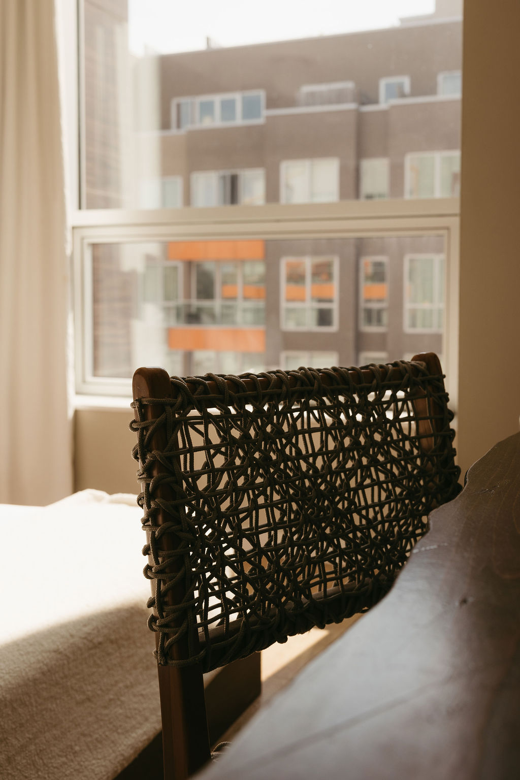 A woven chair by the window, looking out at the building's orange balconies