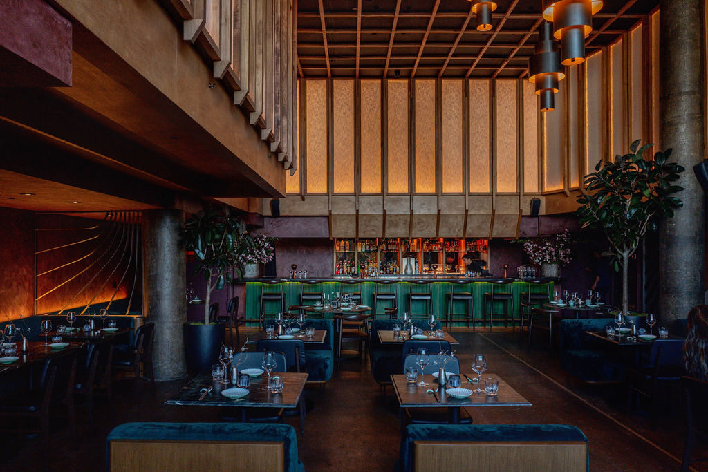 The restaurant dining room at night, with a green bar and blue velvet banquettes