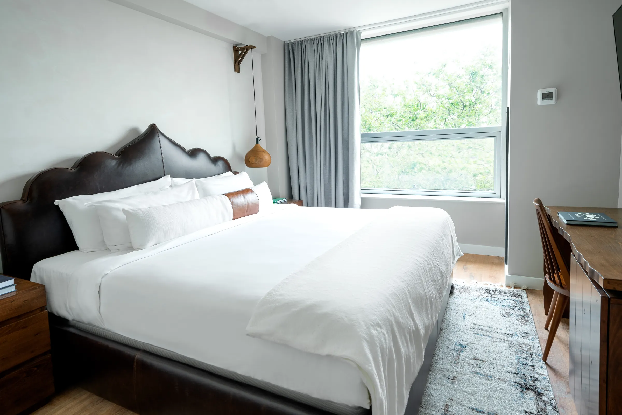 A king room with a scalloped leather headboard and a window onto the trees