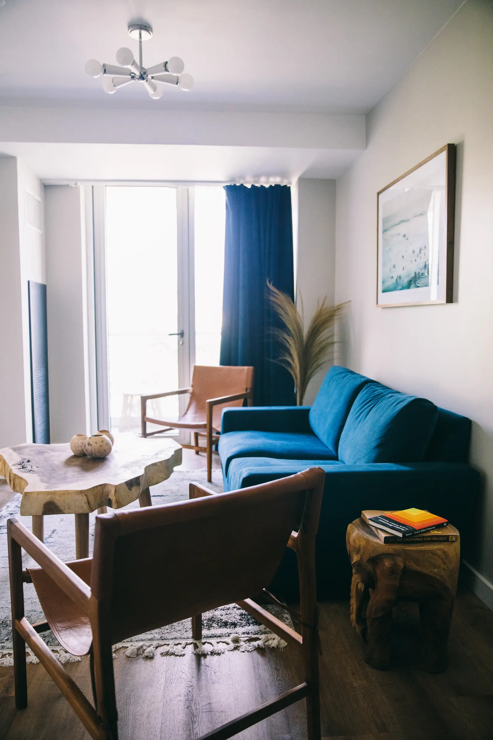 A suite living room with a blue velvet sofa, leather sling chairs and a live-edge table