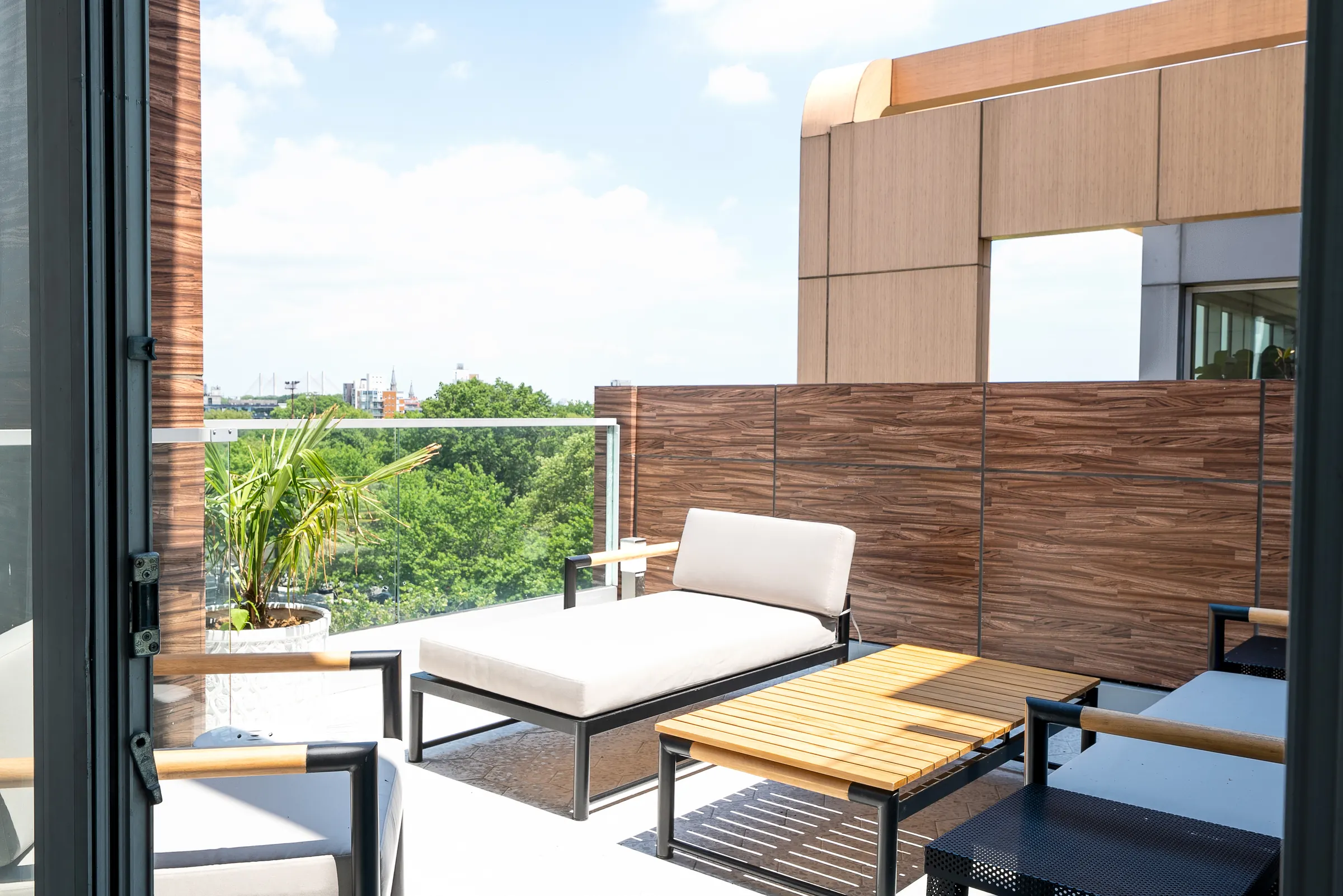 A private balcony with a daybed and slatted wood screen, overlooking treetops