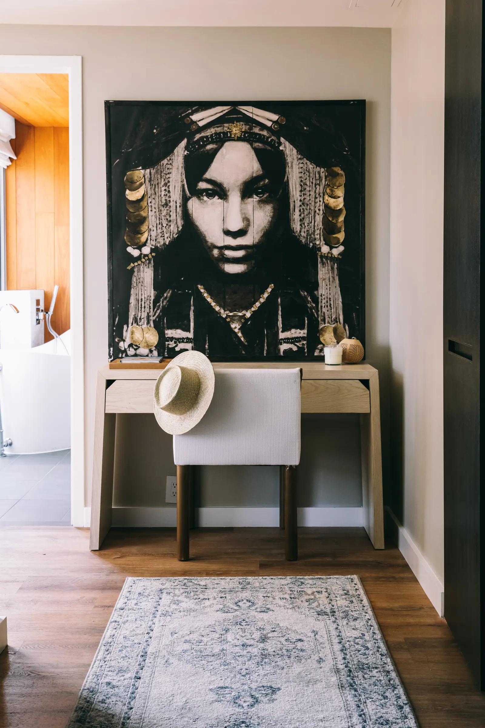 A writing desk below a large portrait canvas, with the bathroom beyond