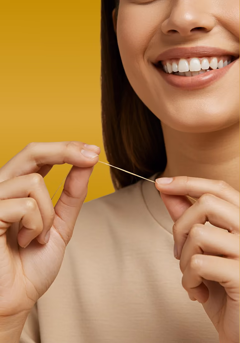 Close-up of a smiling woman holding dental floss between her fingers against a yellow background.