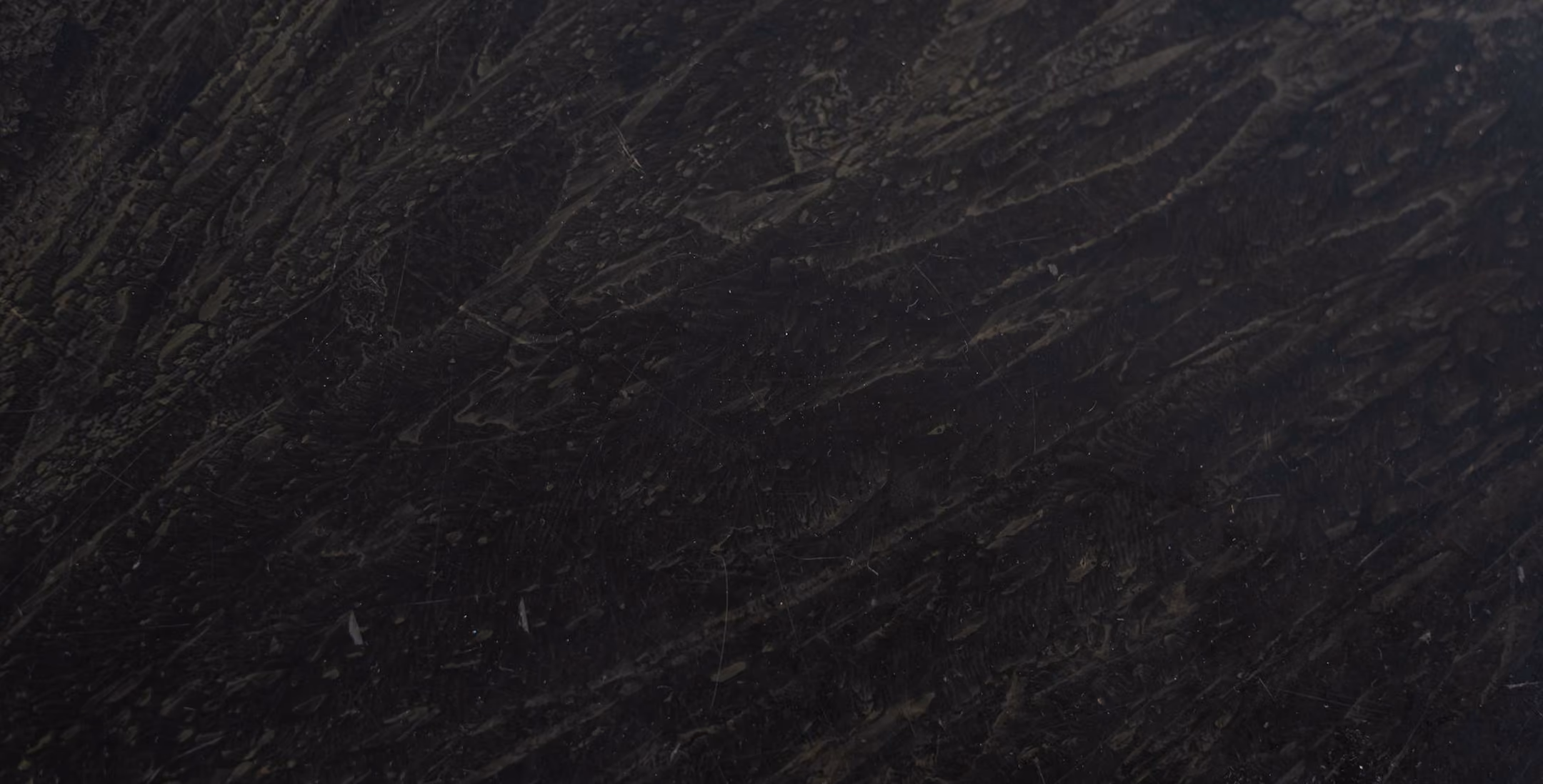 Close-up of black textured surface with subtle thin grayish and dark streaks creating a rough, uneven pattern.