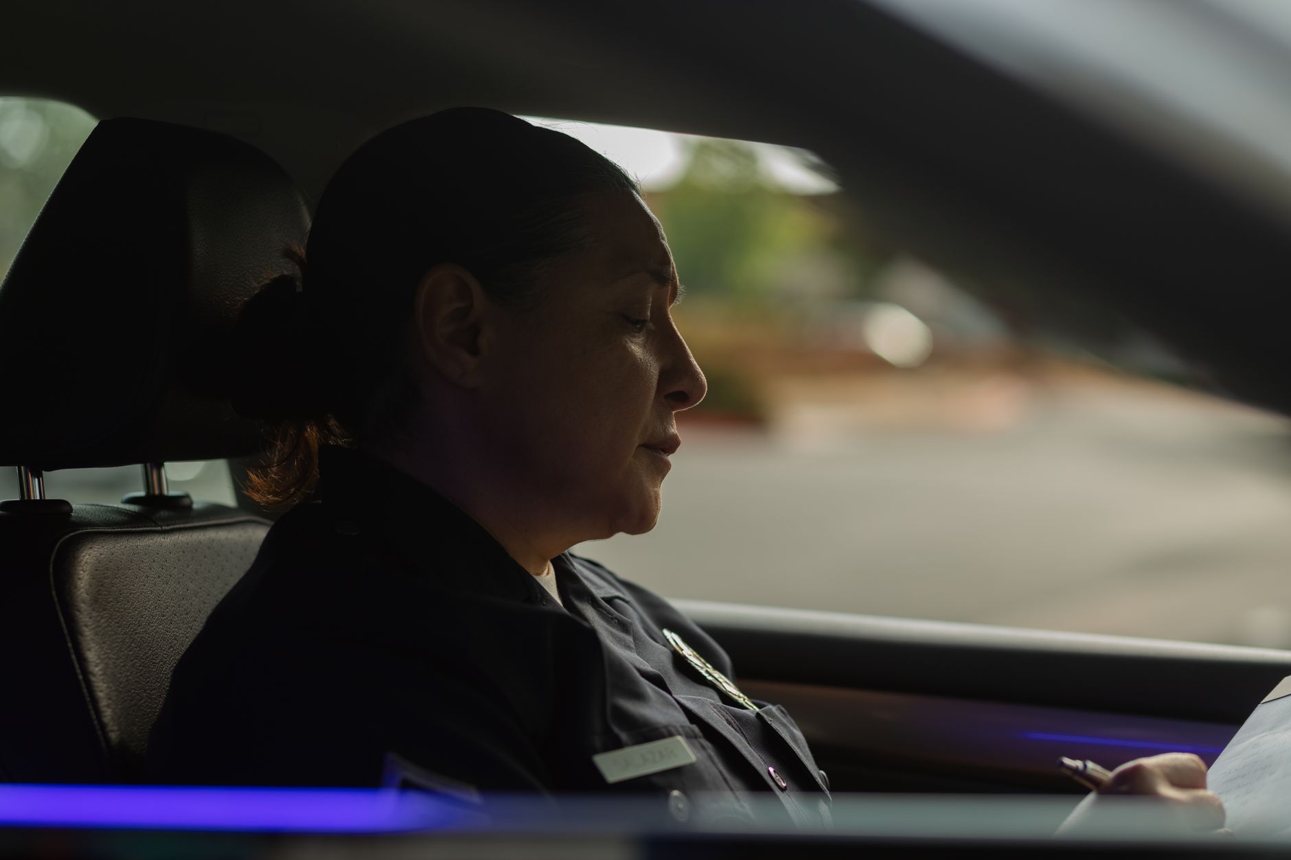 Policewoman in uniform writing notes inside a patrol car during the day.