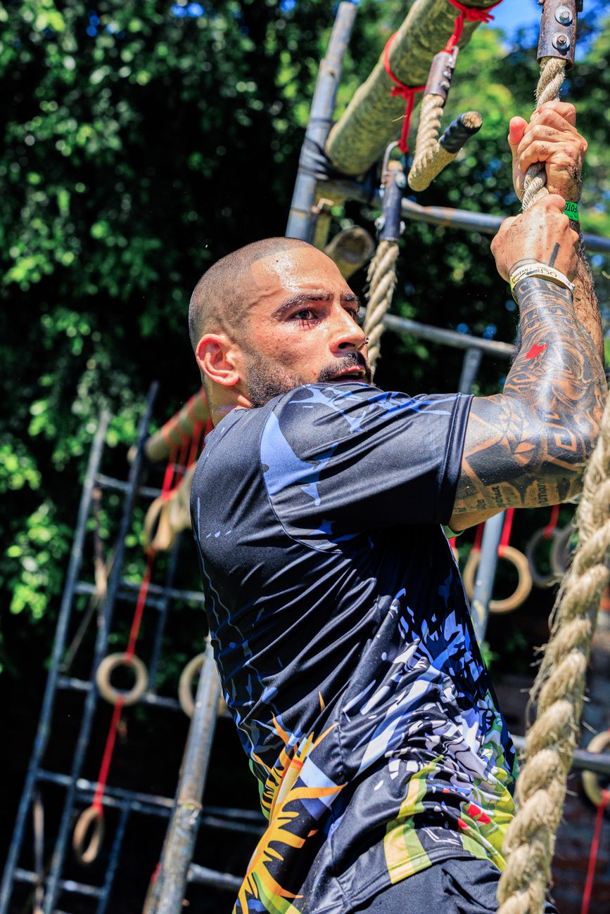 Fit man climbing a rope during an outdoor obstacle course challenge.