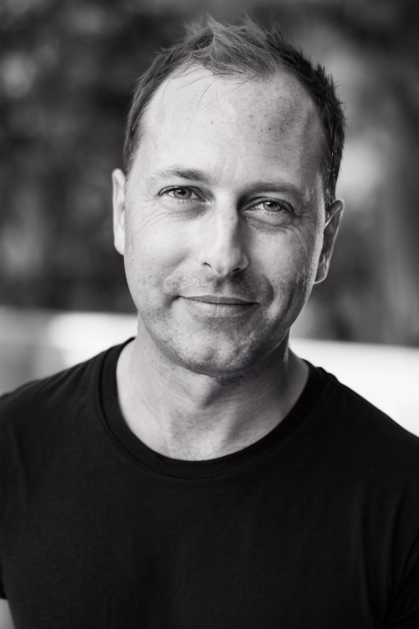 Black and white portrait of a smiling man wearing a black t-shirt with short, tousled hair.