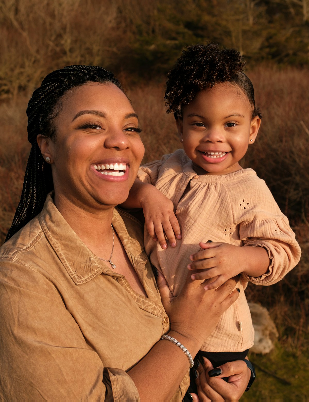A smiling mother holding her young daughter outdoors