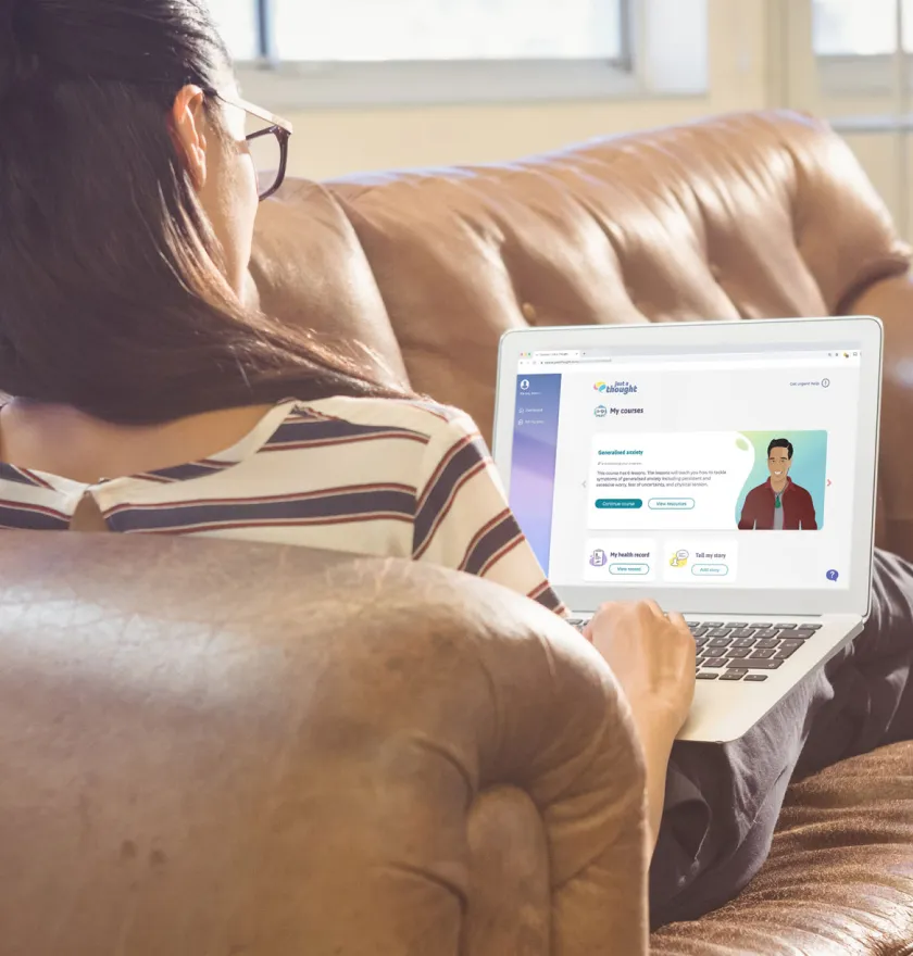 Person wearing glasses sits on a brown leather couch using a laptop with an online course about generalized anxiety on the screen.