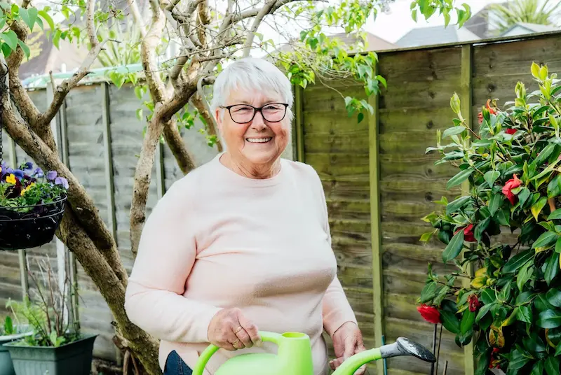 An elderly woman smiling with a watering can