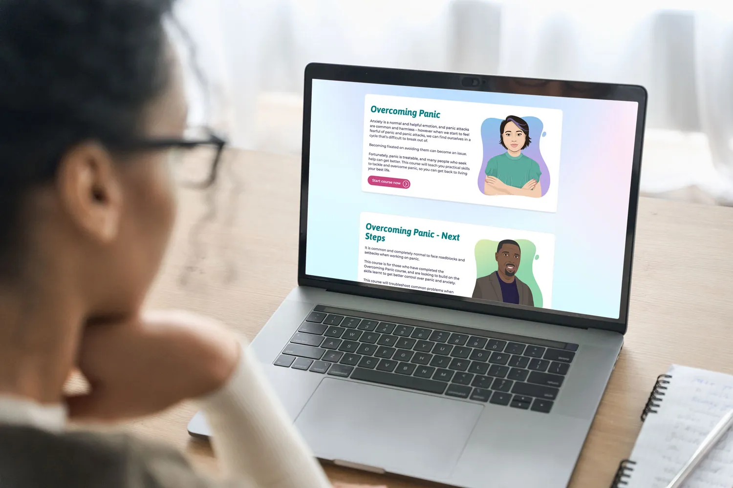 Person looking at a laptop screen displaying two course sections titled 'Overcoming Panic' and 'Overcoming Panic - Next Steps' with illustrated portraits.