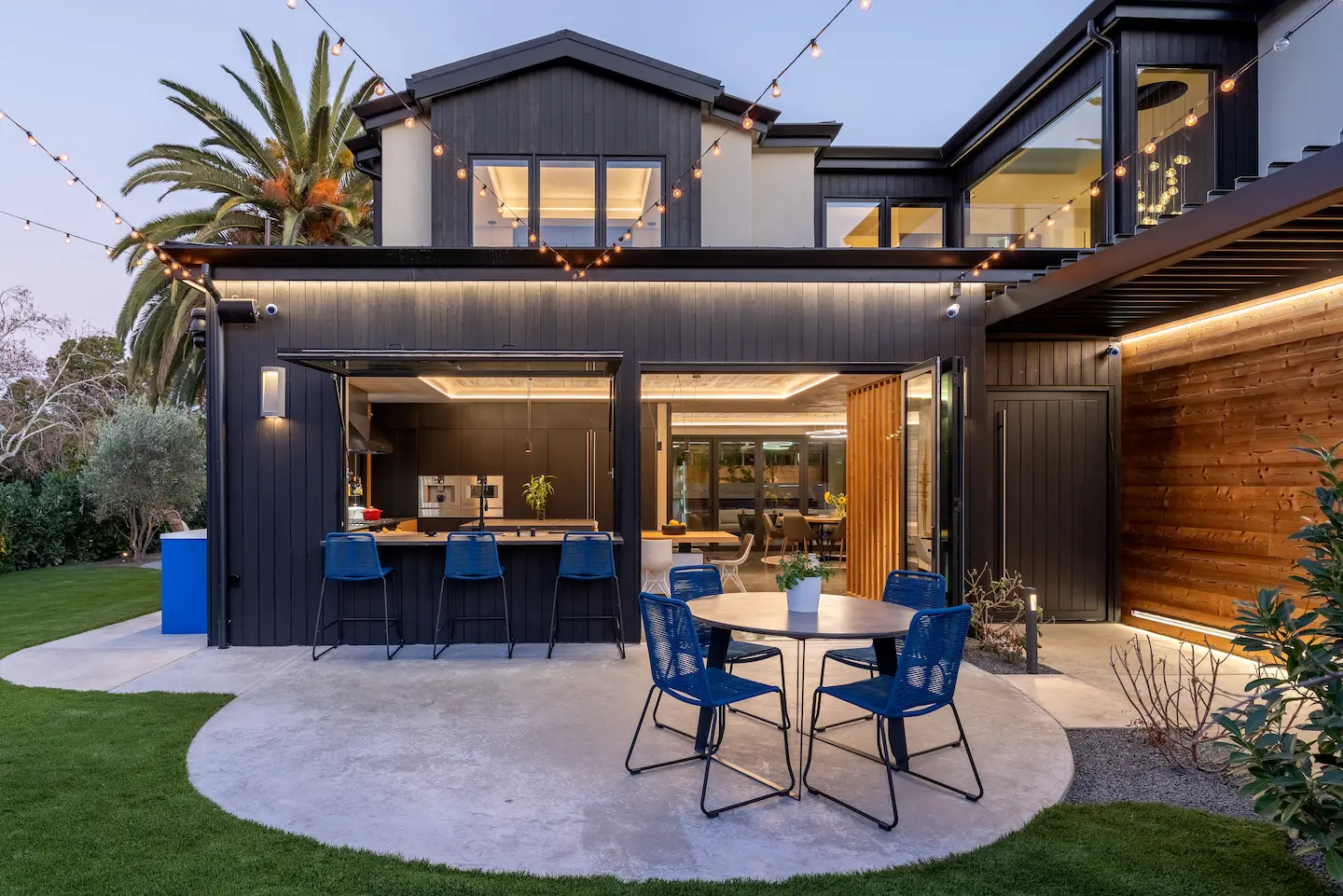 Colorado Avenue new build featuring an outdoor entertaining space at night with string lights, a kitchen bar open to the exterior, and patio seating.