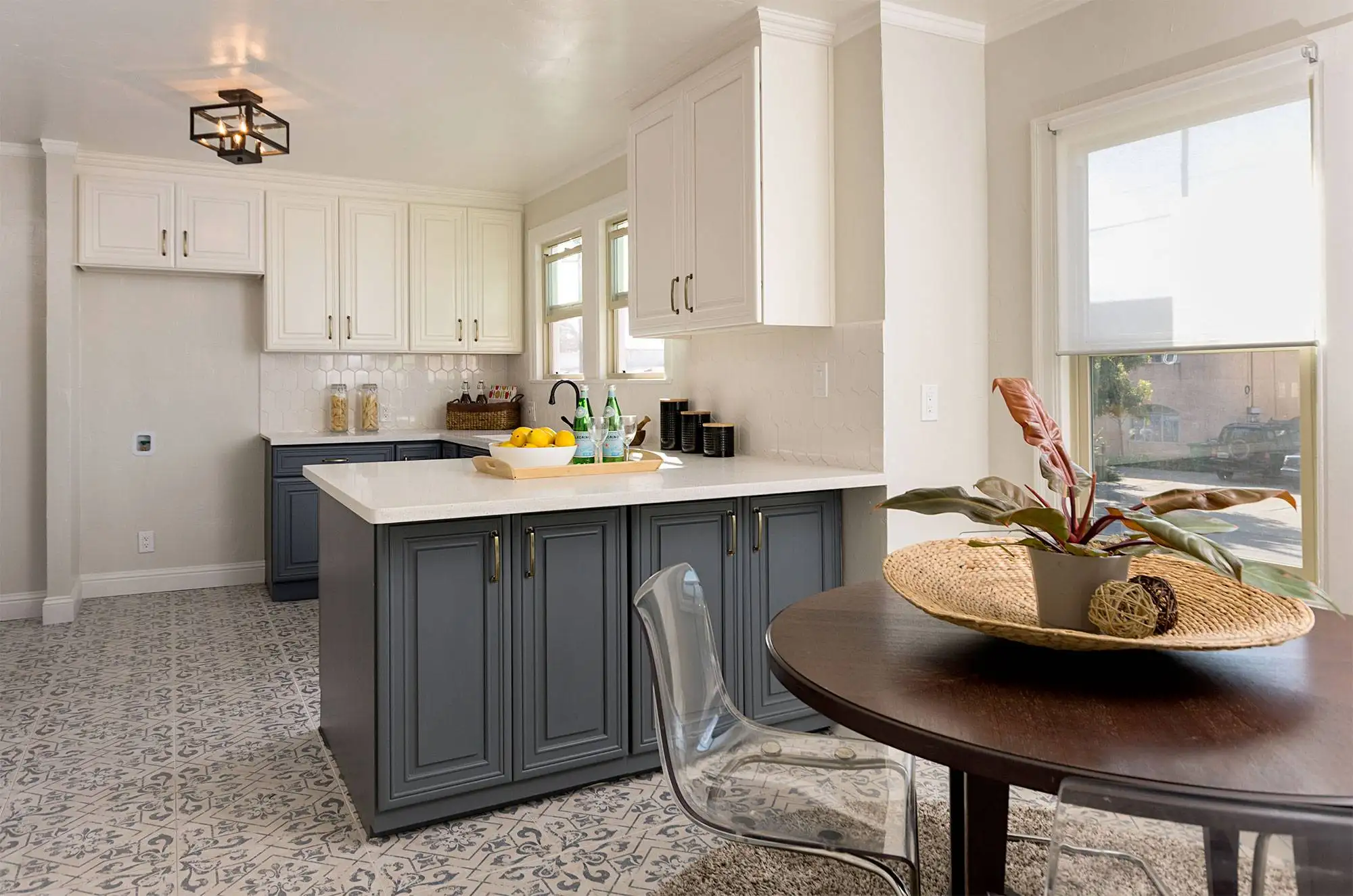 Kitchen interior with white upper cabinets, gray lower cabinets, and a patterned tile floor next to a round dining table